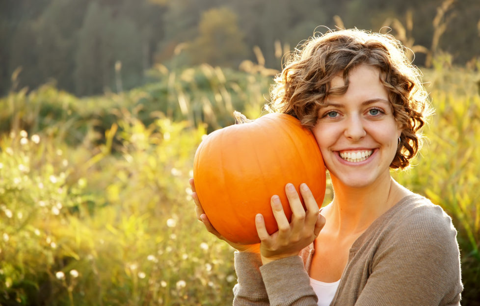 Smiling curly-haired girl holding a pumpkin to her cheek.
