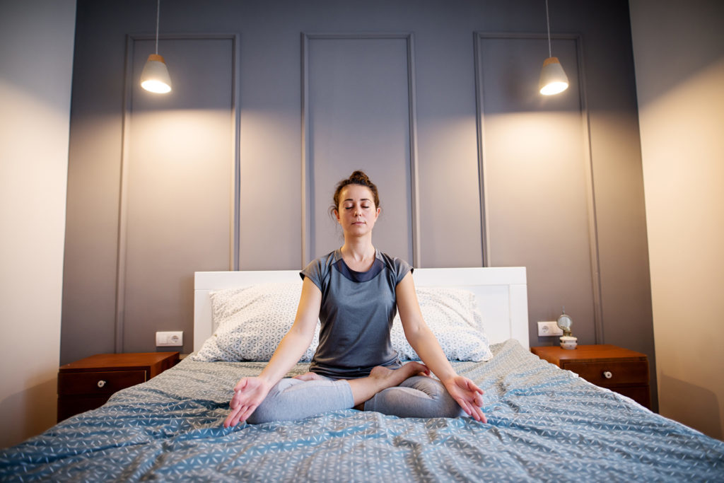 Front view of peaceful attractive middle aged active woman practising yoga on the bed 