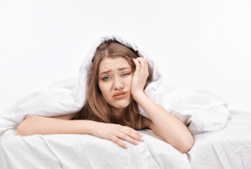 woman at the edge of her bed with negative expression feeling sick and looking at camera displeased.