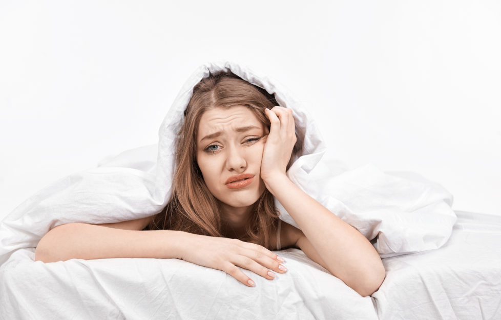 woman at the edge of her bed with negative expression feeling sick and looking at camera displeased.