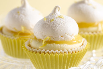 Three lemon meringue cupcakes in yellow cake cases