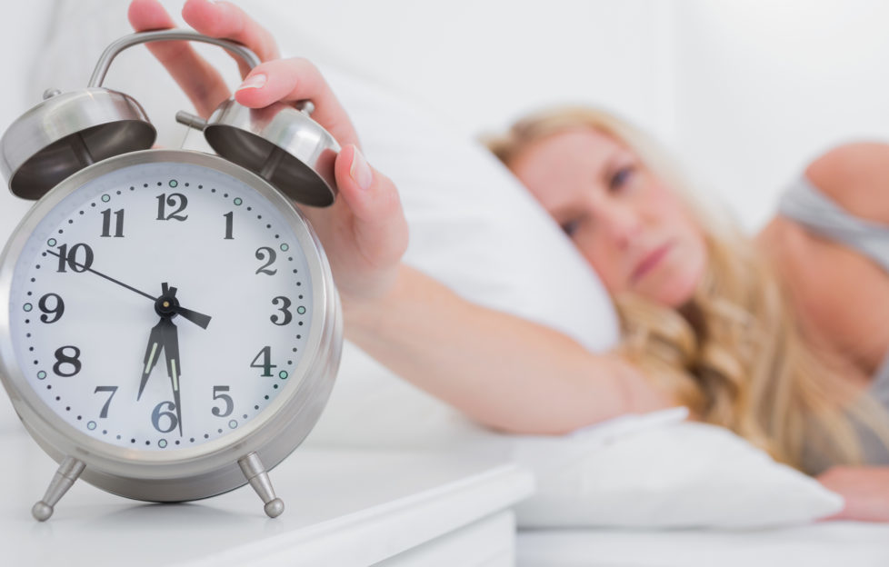 Tired woman turning off the alarm clock in her bed