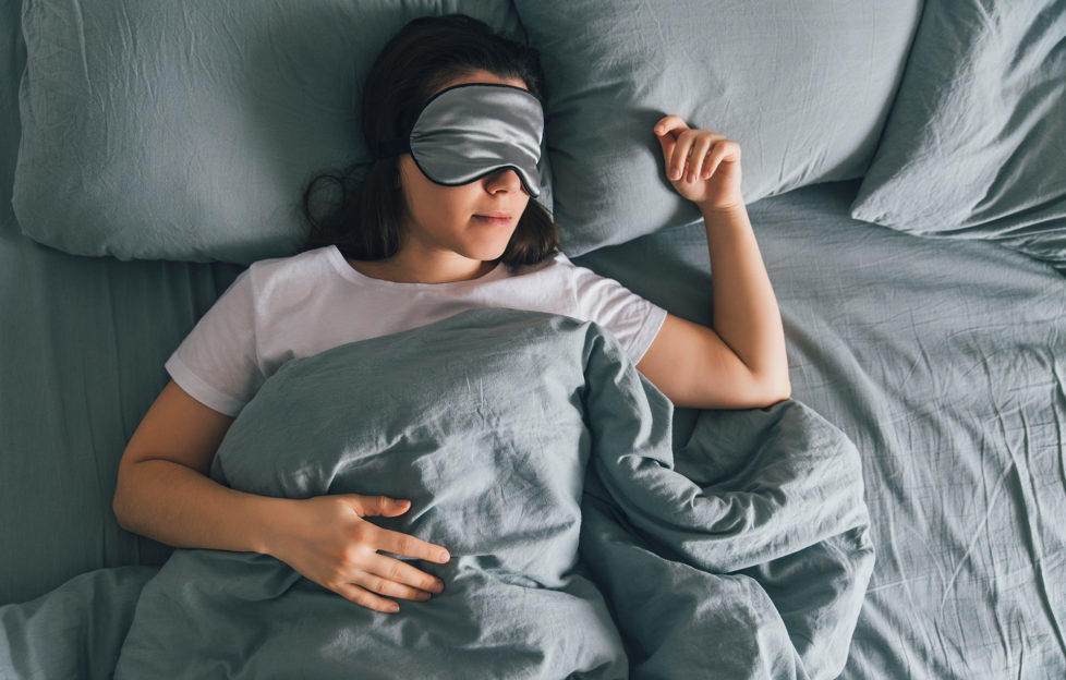 woman sleep in eye patch in grey bed.