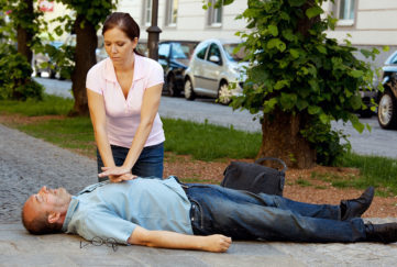 Middle aged man lying in tree lined street, woman doing chest compressions