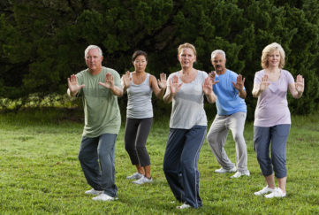 Multi-ethnic group of adults practicing tai chi in park.
