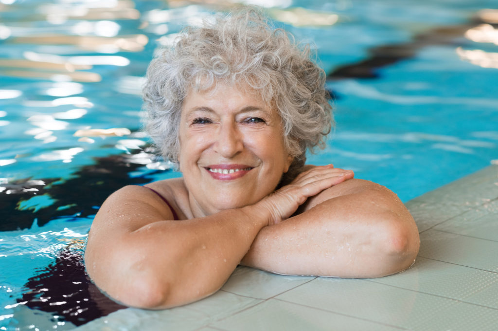 Portrait of elderly woman against the edge of a swimming pool and looking at camera. Fit and active senior woman enjoying retirement in the swimming pool. Beautiful mature woman relaxing in the swimming pool.