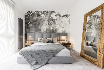 King-size bed with gray square headboard, large rustic wooden mirror and textured wall in trendy minimalist apartment Pic: Istockphoto