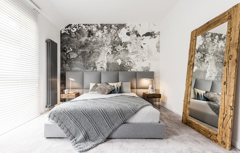 King-size bed with gray square headboard, large rustic wooden mirror and textured wall in trendy minimalist apartment Pic: Istockphoto