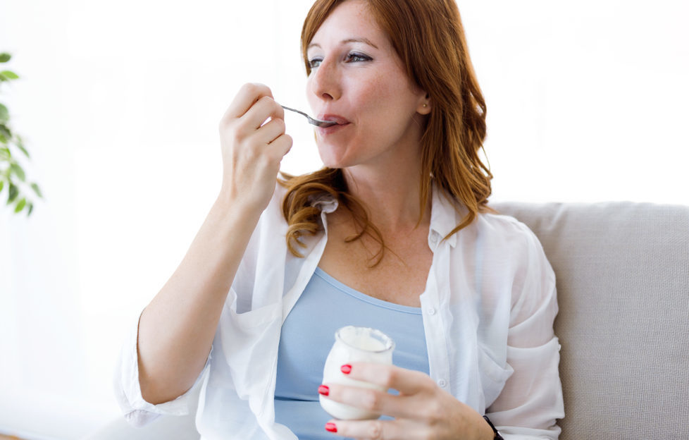 Beautiful young woman eating yogurt at home.