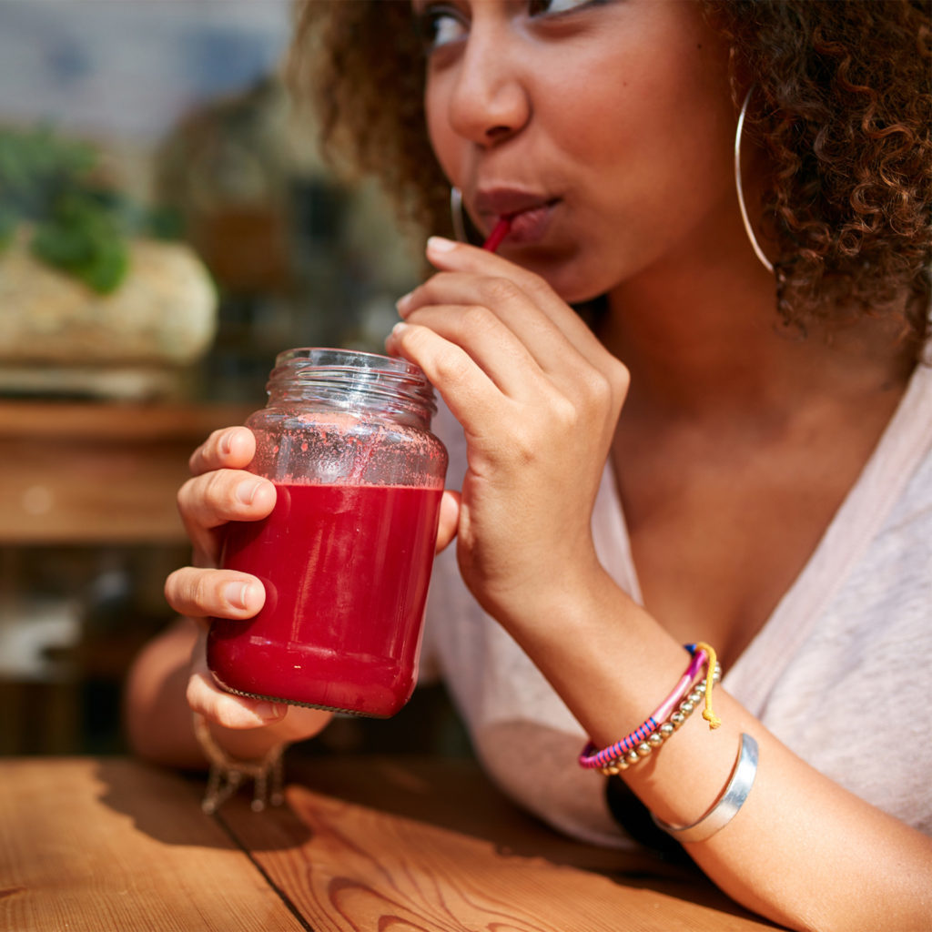 Young mixed race woman drinking deep pink fruit juice drink in a bar