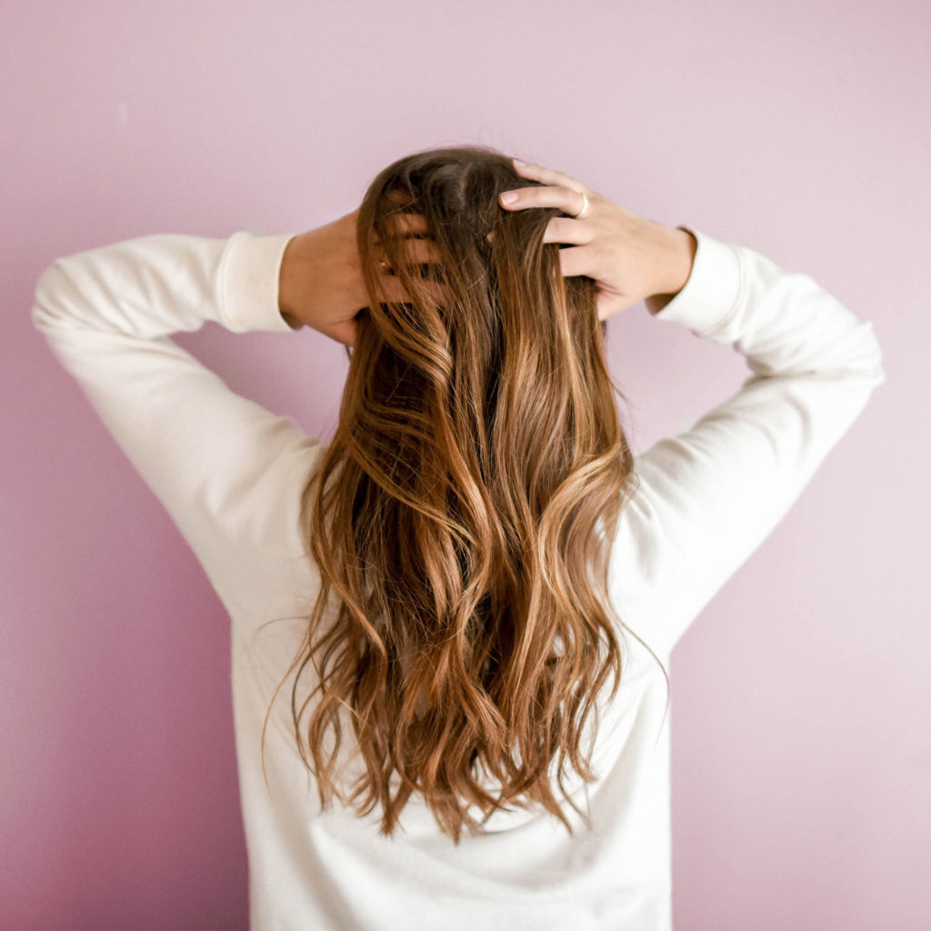 Back view of woman with long tumbling brown hair facing pink painted wall