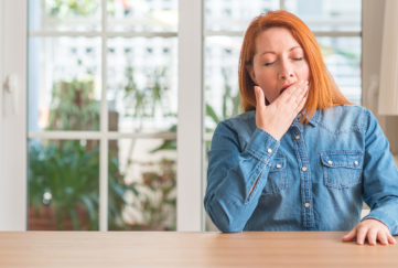Redhead woman at home bored yawning tired covering mouth with hand. Restless and sleepiness.
