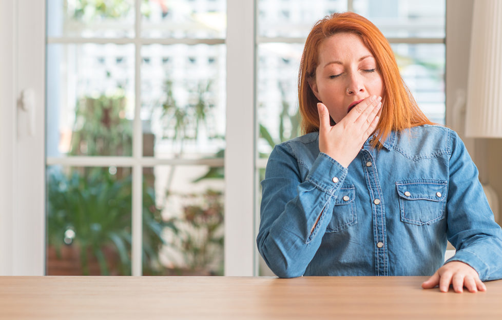 Redhead woman at home bored yawning tired covering mouth with hand. Restless and sleepiness.