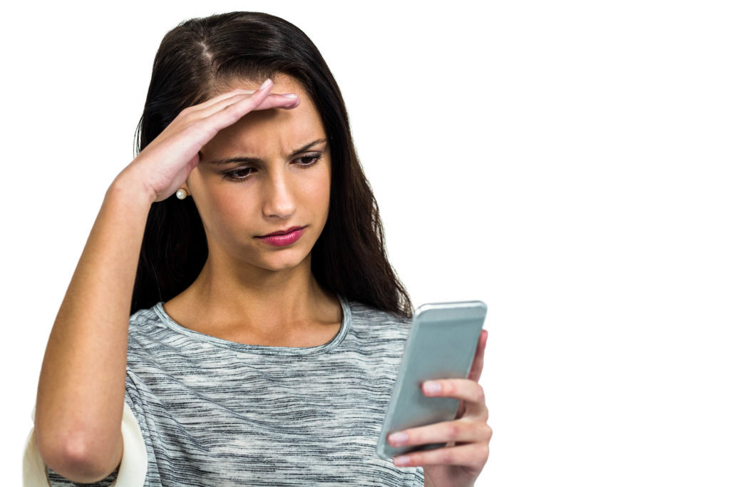 Worried woman with hand on face using smartphone on white screen Pic: Istockphoto