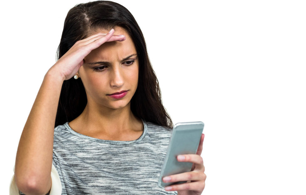 Worried woman with hand on face using smartphone on white screen Pic: Istockphoto