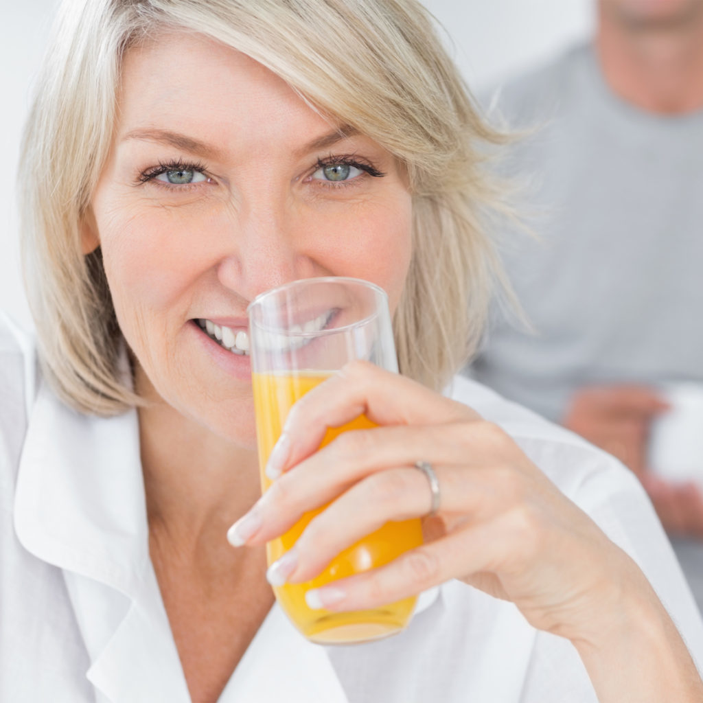 Happy woman drinking orange juice in kitchen with partner standing behind