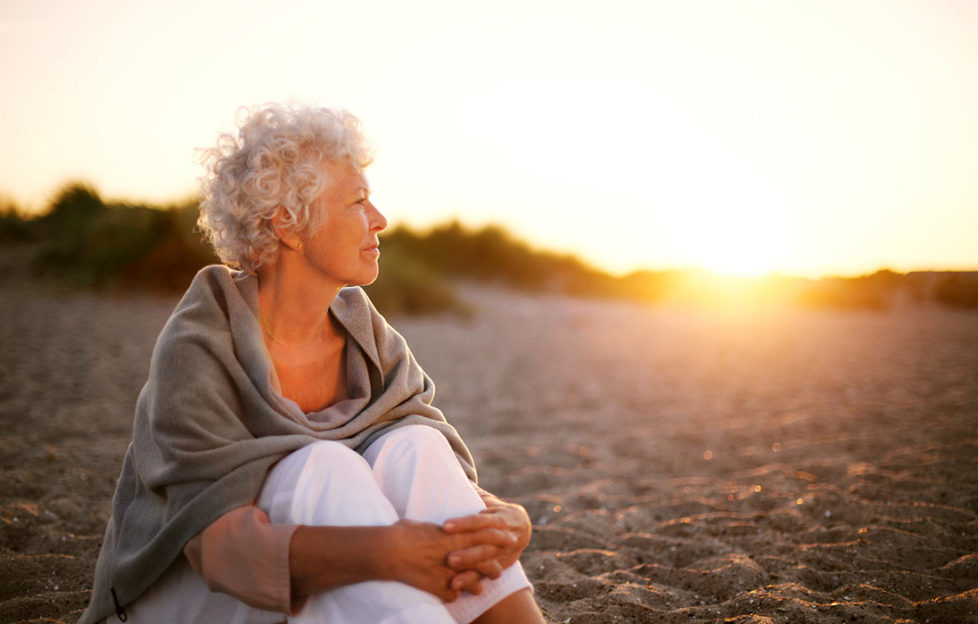 Mature woman with wrap shawl sitting on beach enjoying sunset