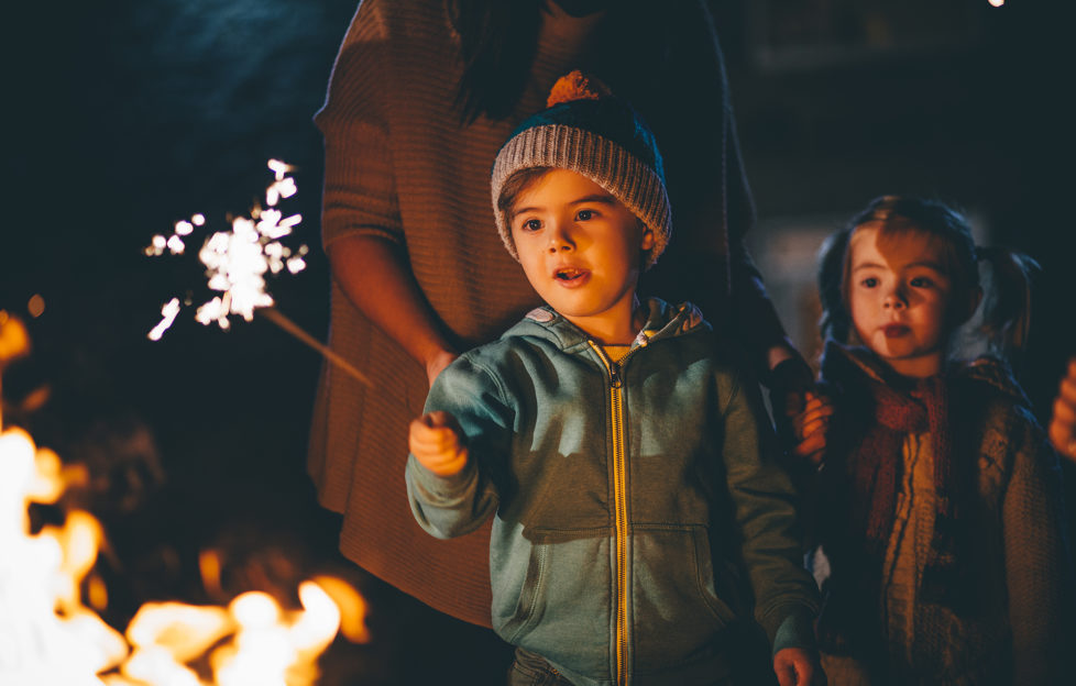 Little boy playing with a sparkler in front of a bonfire on November 5th for Bonfire Night.