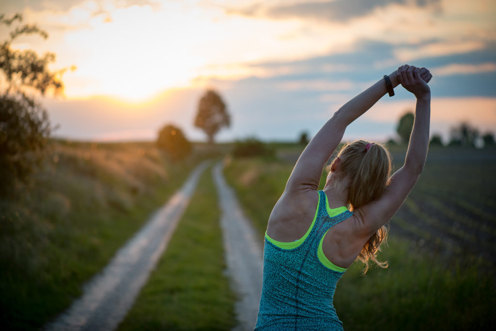 Happy successful sportswoman raising arms to the sky on golden back lighting sunset summer. Fitness athlete with arms up celebrating goals after sport exercising and working out outdoors.
