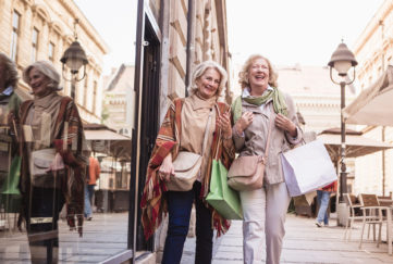 Two senior ladies in shopping. Talking, laughing carrying shopping bags.