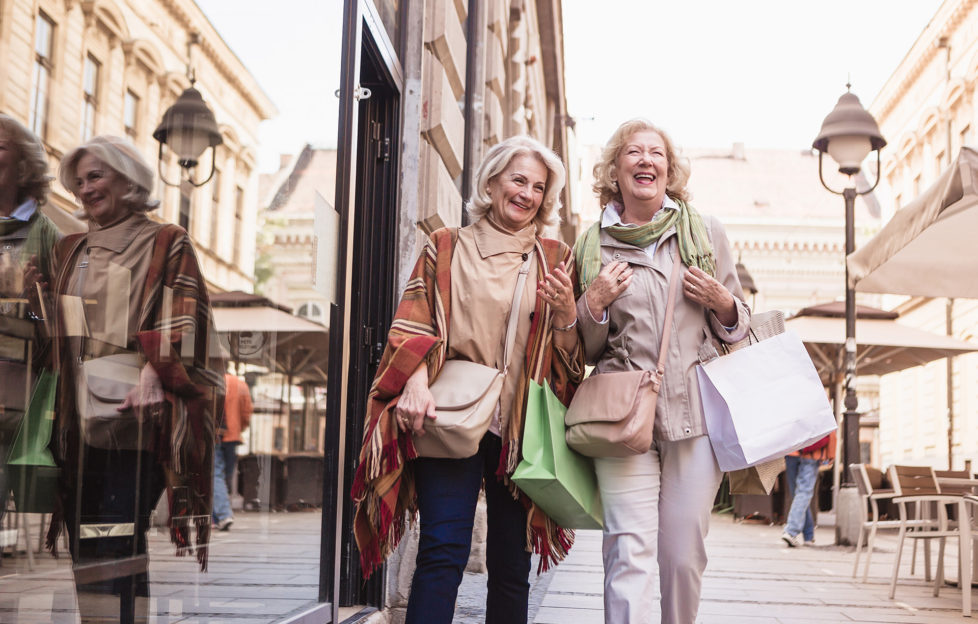 Two senior ladies in shopping. Talking, laughing carrying shopping bags.