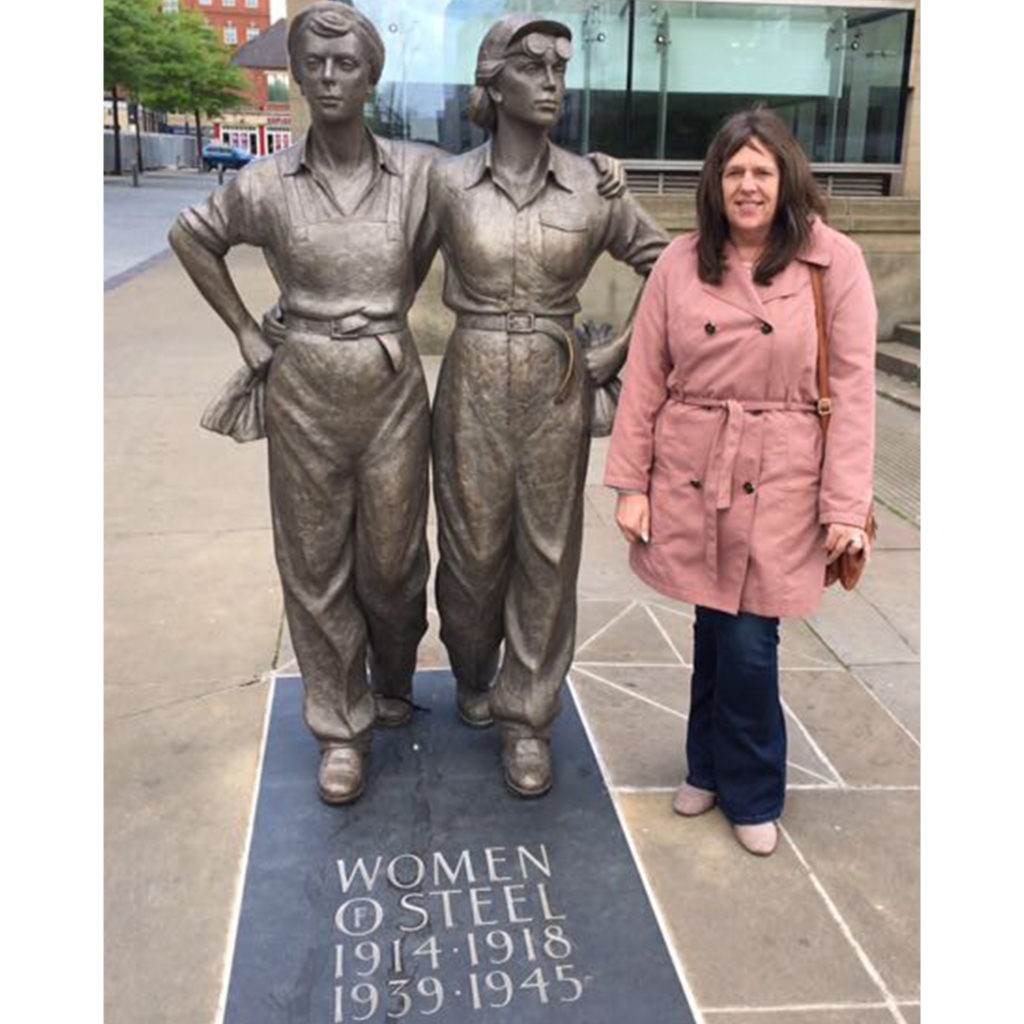 Woman standing beside two bronze statues of female wartime workers