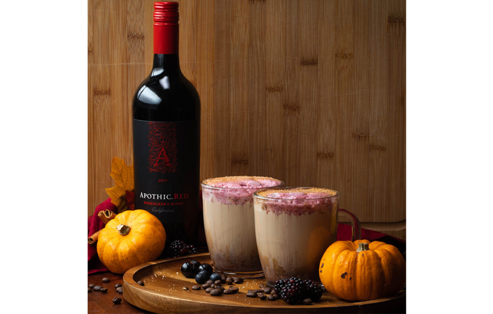 Bottle of Apothic red wine, 2 cups of latte with red drizzle on top on round wooden board with miniature pumpkins and berries