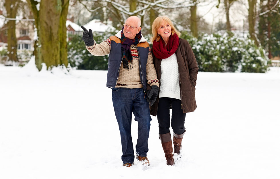 Image of elderly couple walking together in snow park on a winter day