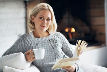 A young woman enjoying her novel with a hot drink while sitting inside near a fireplace Pic: Istockphoto