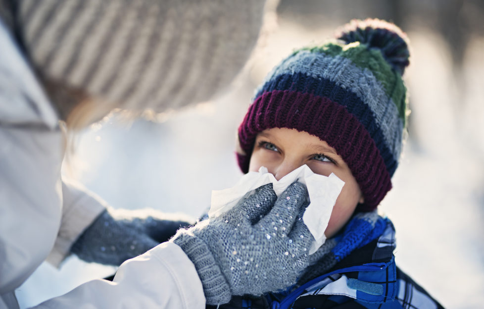 Mother and son having winter walk. Mother is blowing nose of her sick son.