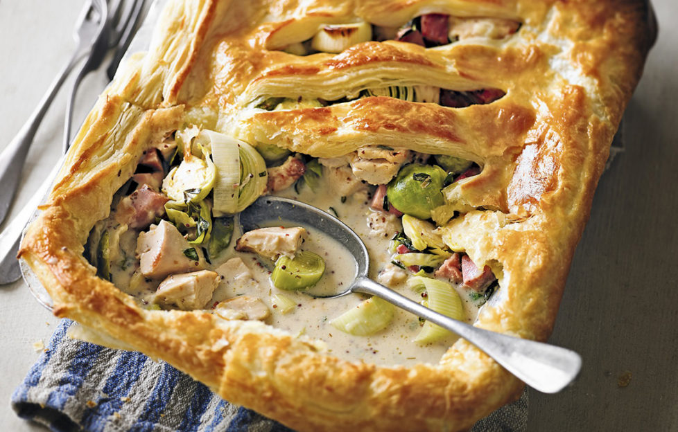 Golden puff pastry pie made of Christmas leftovers in dish, one portion served showing meat and vegetables in creamy sauce