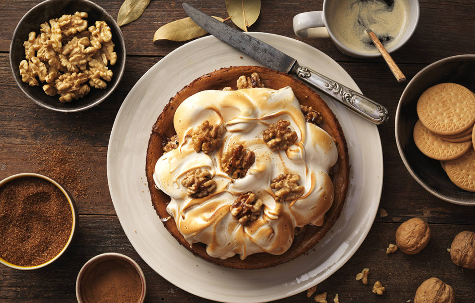 Cheesecake topped with meringue, sprinkled with caramelised walnuts, with small pots of spices around