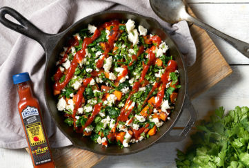 Black iron skillet filled with spinach, sweet potato, feta with a zigzag drizzle of red sauce