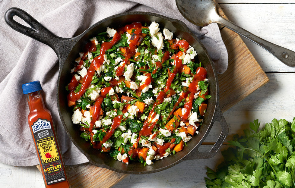 Black iron skillet filled with spinach, sweet potato, feta with a zigzag drizzle of red sauce