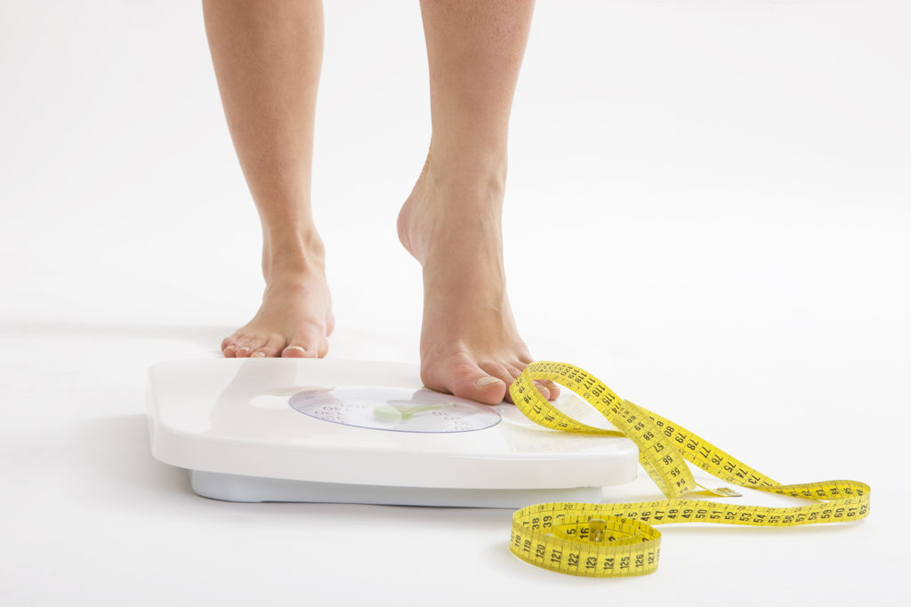 Woman's feet standing on scales with tape measure lying on ground