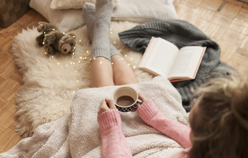 Girl doing hygge with warm blanket, coffee and reading book Pic: Istockphoto