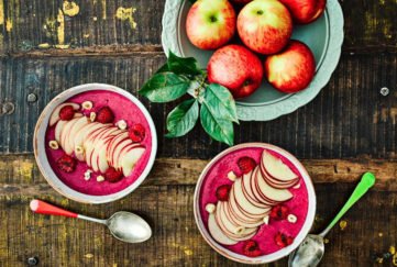 Two bowls of bright magenta smoothie decorated with fanned apple and hazelnuts