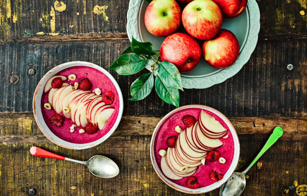 Two bowls of bright magenta smoothie decorated with fanned apple and hazelnuts