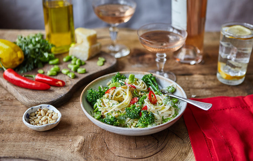 Bowl of spaghetti with creamy sauce and green broccoli, small dish of pine nuts on the side