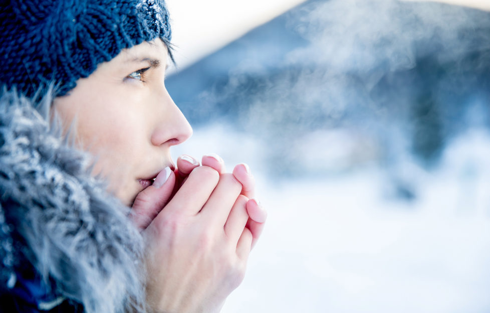 Young woman portrait on a cold winter day. Overcast and cold weather. She is heating her hands with her hot breath.