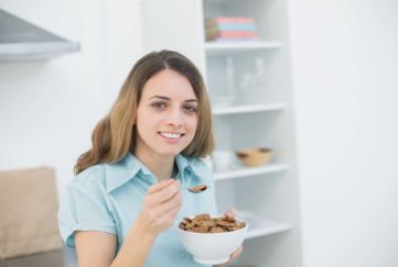Cute woman holding a bowl with cereals while smiling at camera