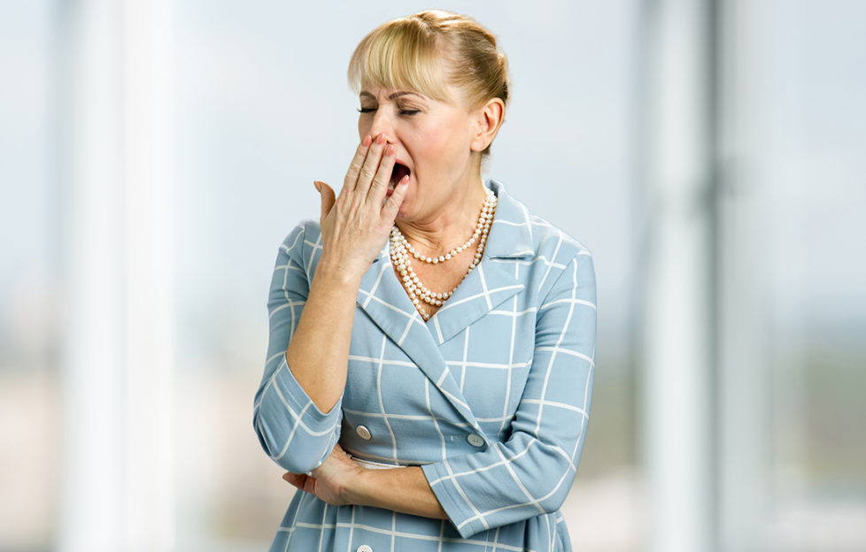 Woman in smart sky-blue and cream suit yawning with tiredness, hand to her mouth
