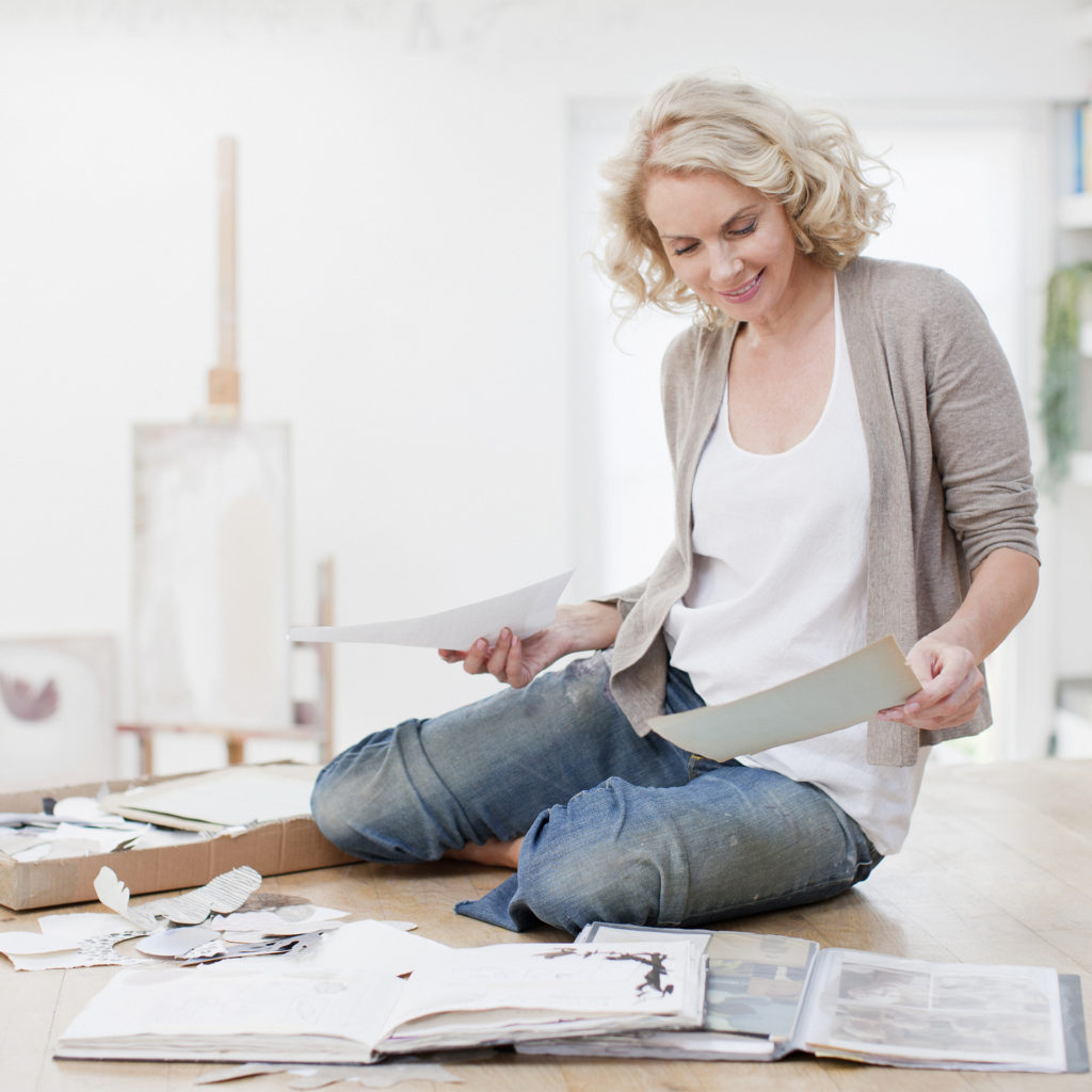 Woman in jeans sitting on floor sorting piles of paper