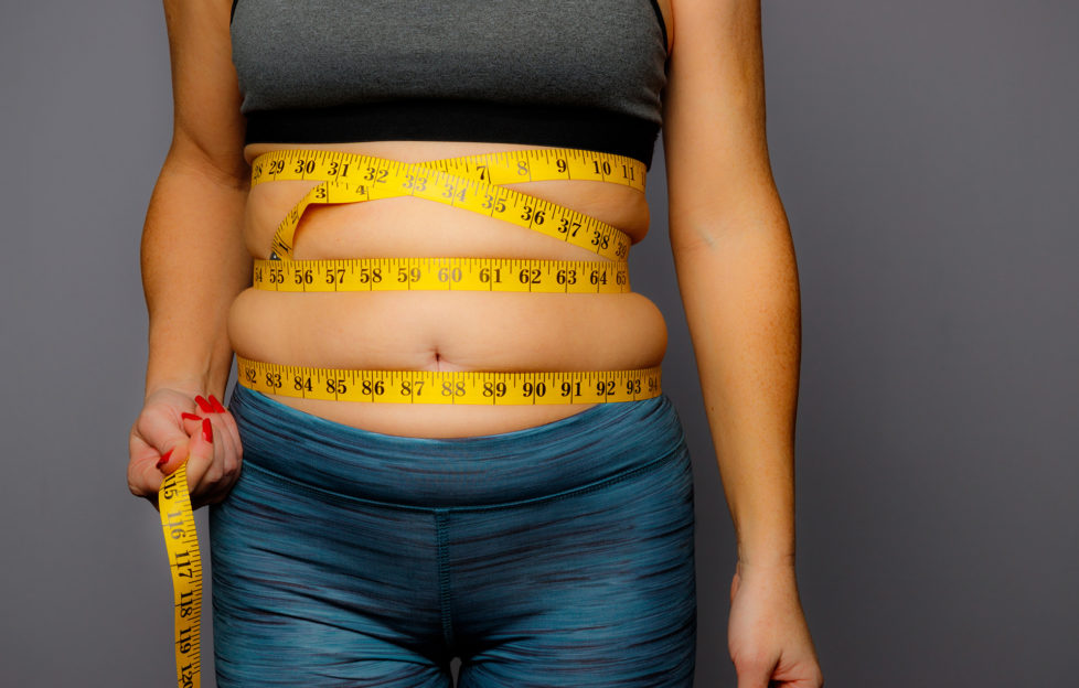 Woman in Active Wear With Squeezed Measuring Tape on a Gray BackgroundWoman in Active Wear With Squeezed Measuring Tape on a Gray Background