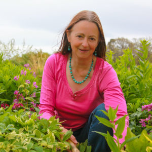 Gardening expert Susie White kneeling amongst bright pink flowering plants which match her top
