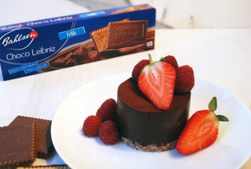 Rich chocolate tart decorated with strawberries and raspberries, with a packet of Bahlsen Choco Leibniz biscuits