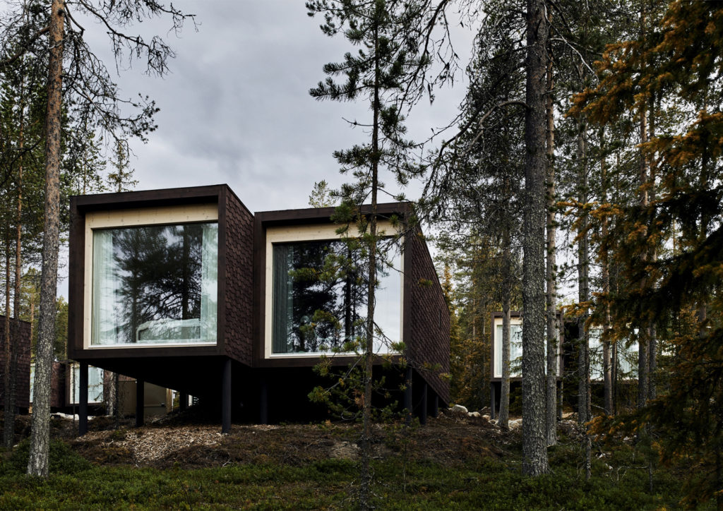 Modern building, looks like two cubes with a window fillimg the ends facing camera, surrounded by pine trees