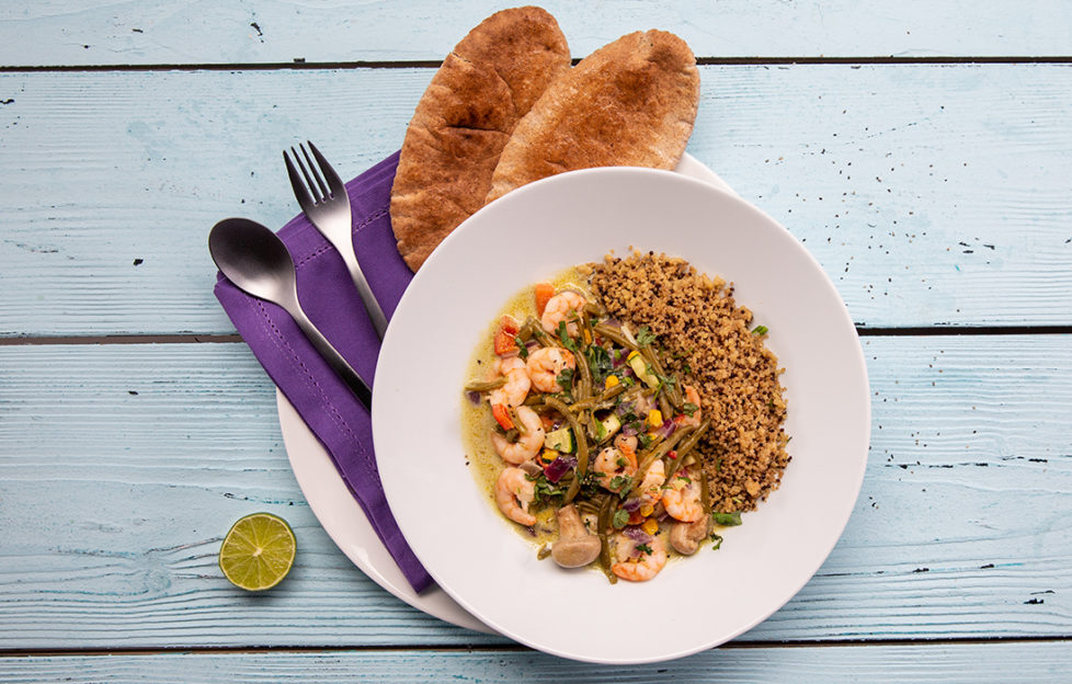 Bowl of green Thai prawn curry with brown rice, toasted mini naan bread and half a lime