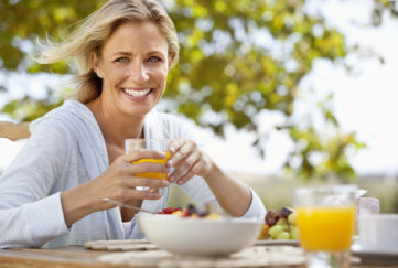 Smiling mature woman with orange juice at breakfast table outdoors