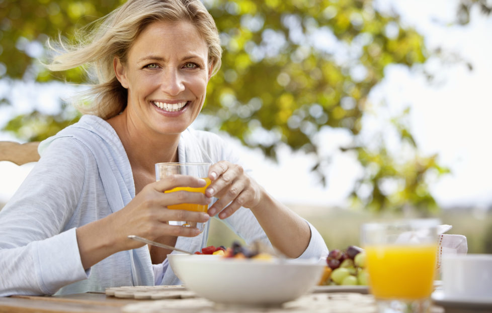 Smiling mature woman with orange juice at breakfast table outdoors